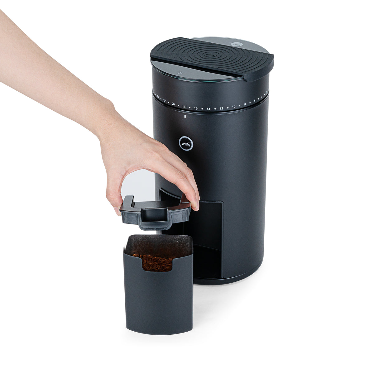 A hand placing the grounds container into the Wilfa Uniform Evo black coffee grinder.