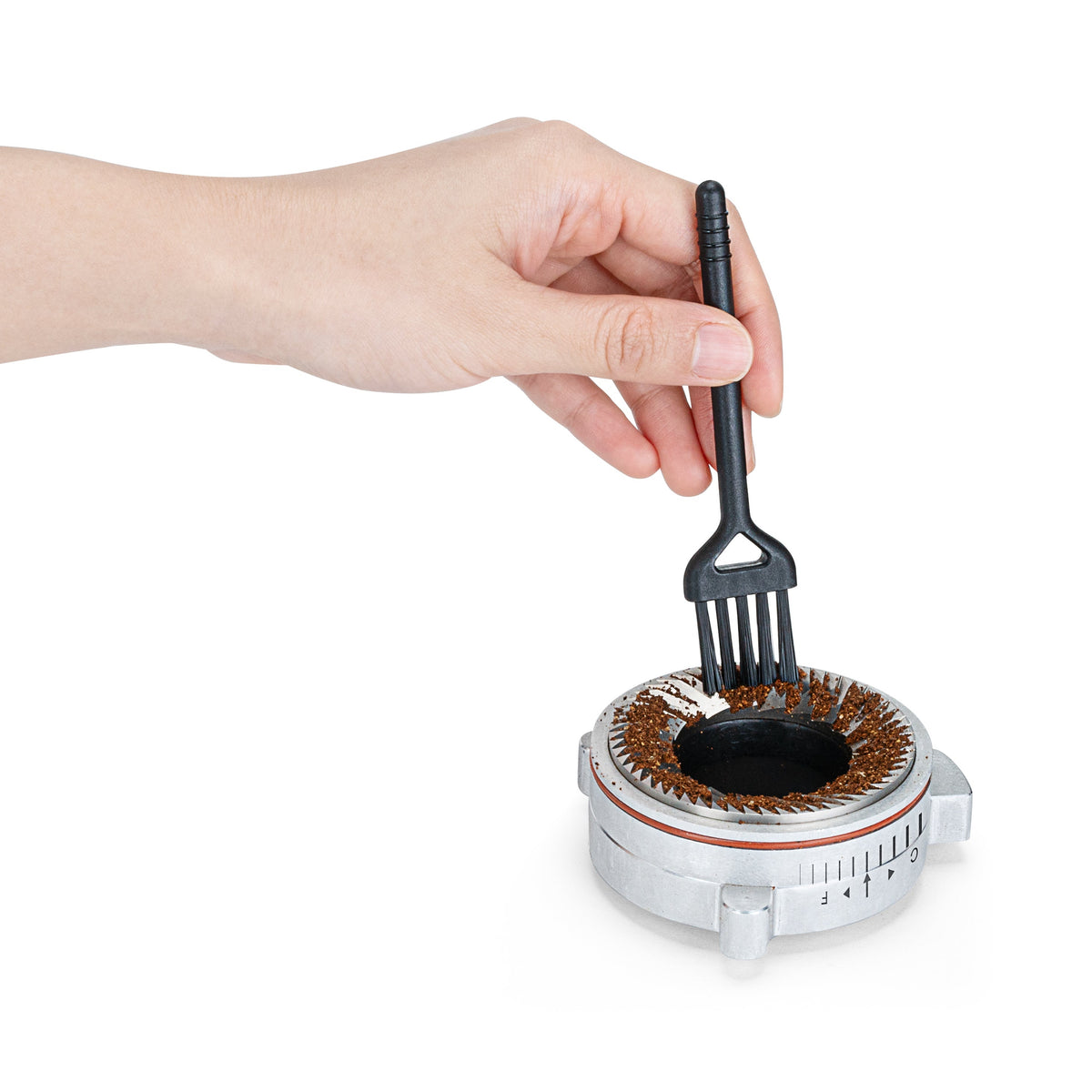 A hand using a cleaning brush to remove coffee grounds from the grinding burr of the Wilfa Uniform Evo coffee grinder.