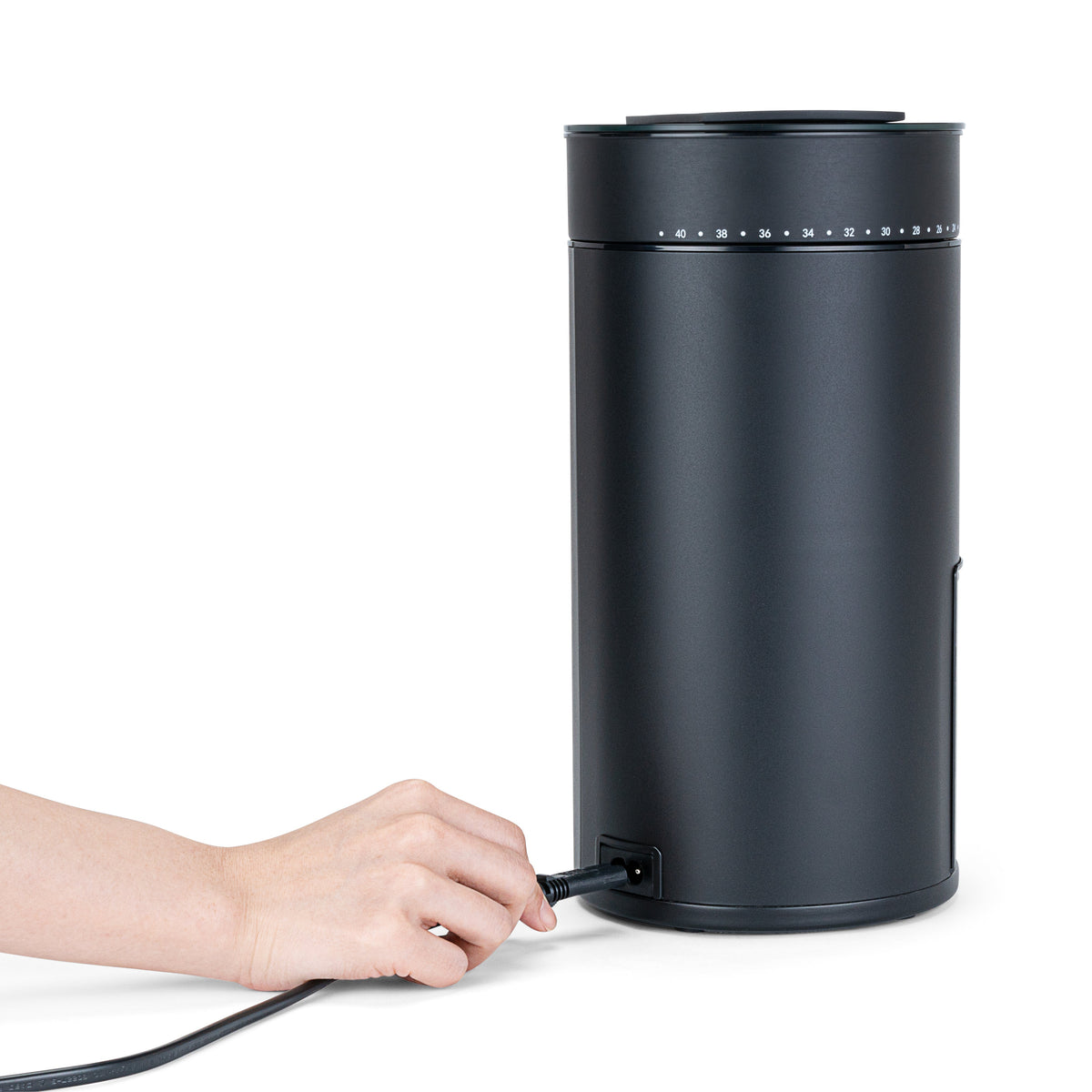A hand plugging the power cord into the back of the Wilfa Uniform Evo black coffee grinder.