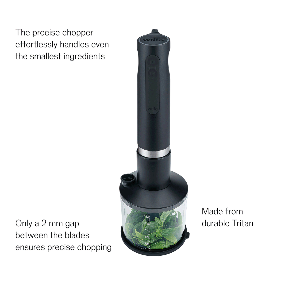 Wilfa Prostick immersion blender with the chopper attachment chopping herbs while oil is poured in, labeled: precise chopper, easy to add liquid, only a 2 mm gap between the blades, made from durable Tritan.