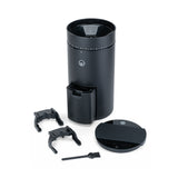 Wilfa Uniform Evo black coffee grinder with its accessories laid out: two portafilter forks, grounds container, lid and cleaning brush.