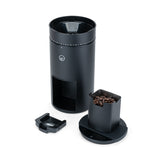 Wilfa Uniform Evo black coffee grinder with the bean hopper filled with coffee beans, shown next to the grounds container and portafilter fork.