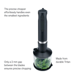 Wilfa Prostick immersion blender with the chopper attachment chopping herbs while oil is poured in, labeled: precise chopper, easy to add liquid, only a 2 mm gap between the blades, made from durable Tritan.
