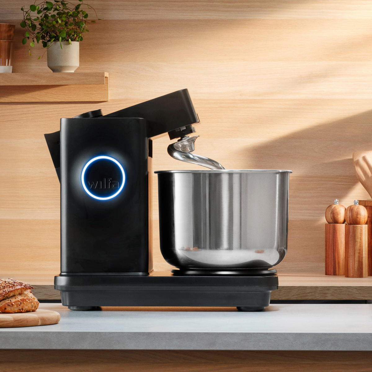 Probaker NXT stand mixer with its illuminated wilfa dial on a kitchen counter, beside fresh bread and a plant.